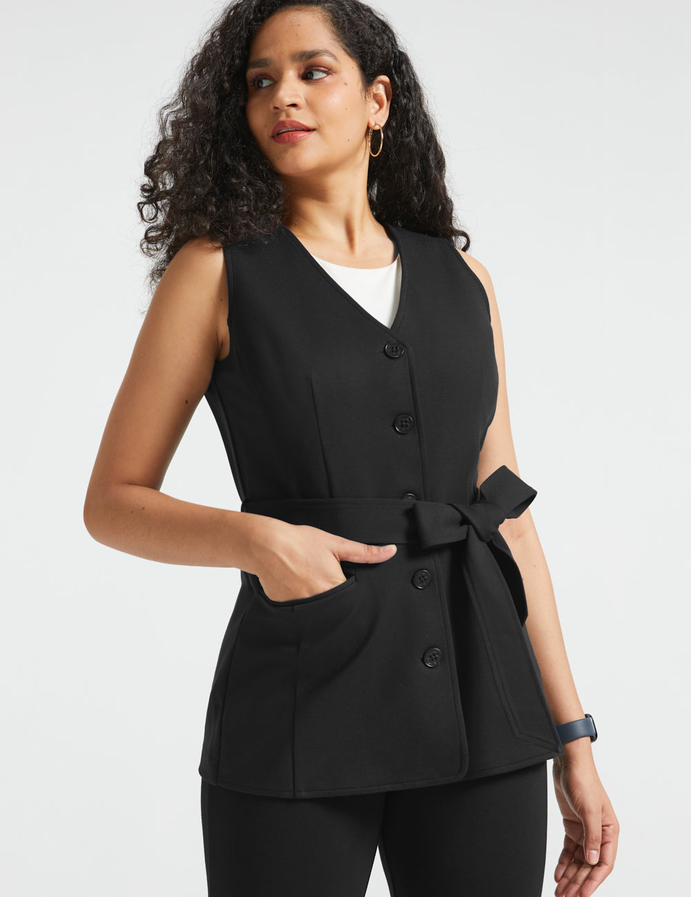 Woman wearing black button-front ponte vest with V-neckline, tie waist and hand in front pocket