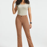 A woman modeling brown and beige checkered flared trousers, standing against a light gray studio background.